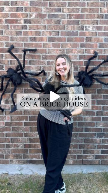 a woman standing in front of a brick wall with black spider decorations on her arms