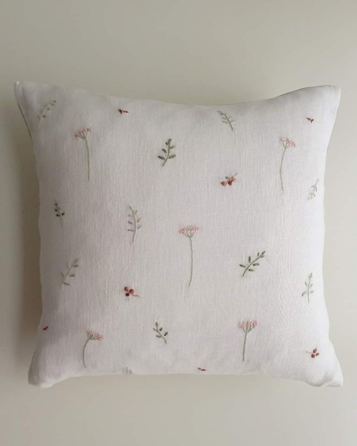 a white pillow with pink and green flowers on the front, sitting against a wall