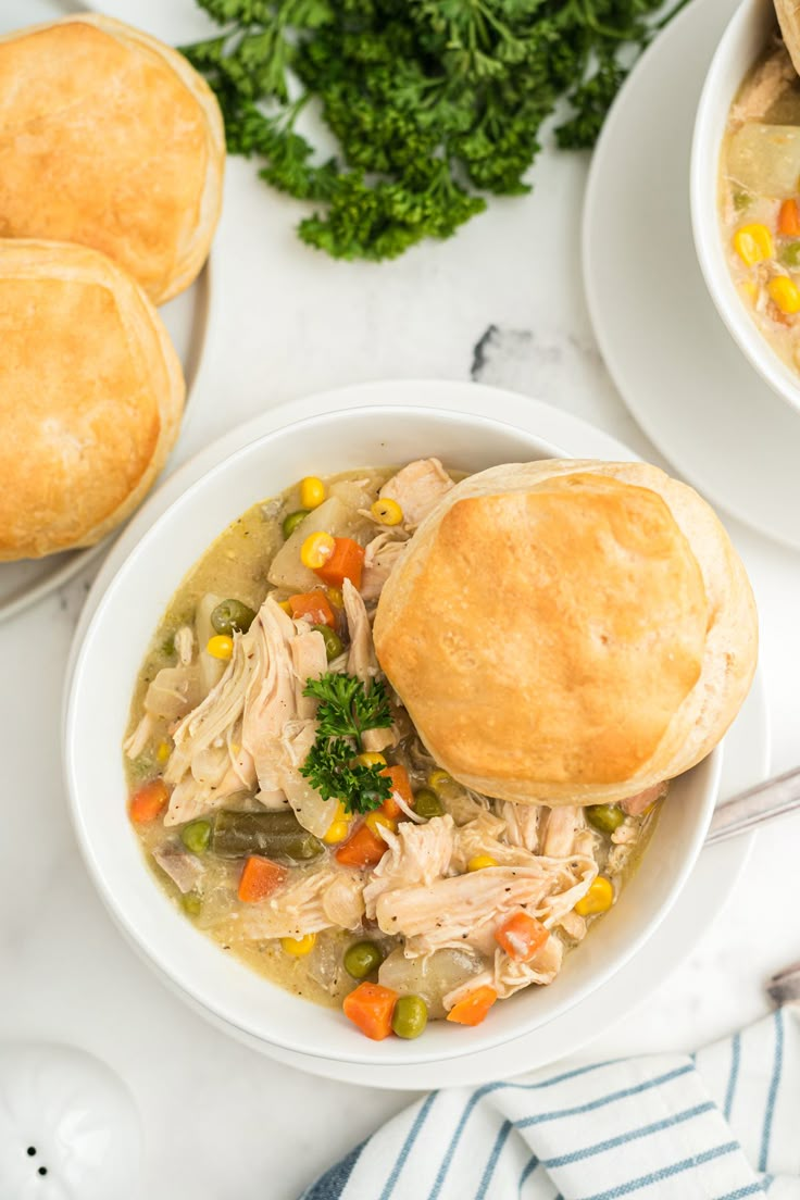 two bowls of chicken pot pie soup on a marble table with bread rolls and parsley