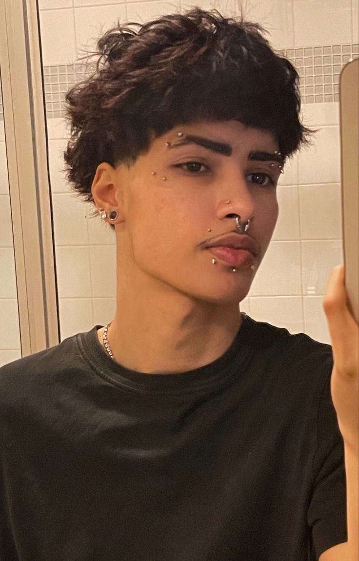 a young man with piercings on his nose looking at himself in the bathroom mirror