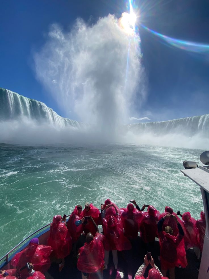 a group of people on a boat in the water near a large waterfall with mist coming out of it