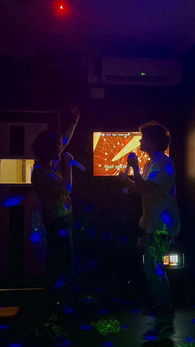 two people are standing in front of a television with their hands up and one person is holding a microphone