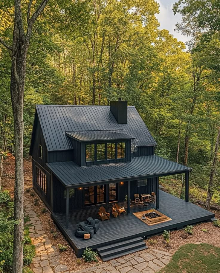 a black house in the woods surrounded by trees and rocks, with an outdoor deck