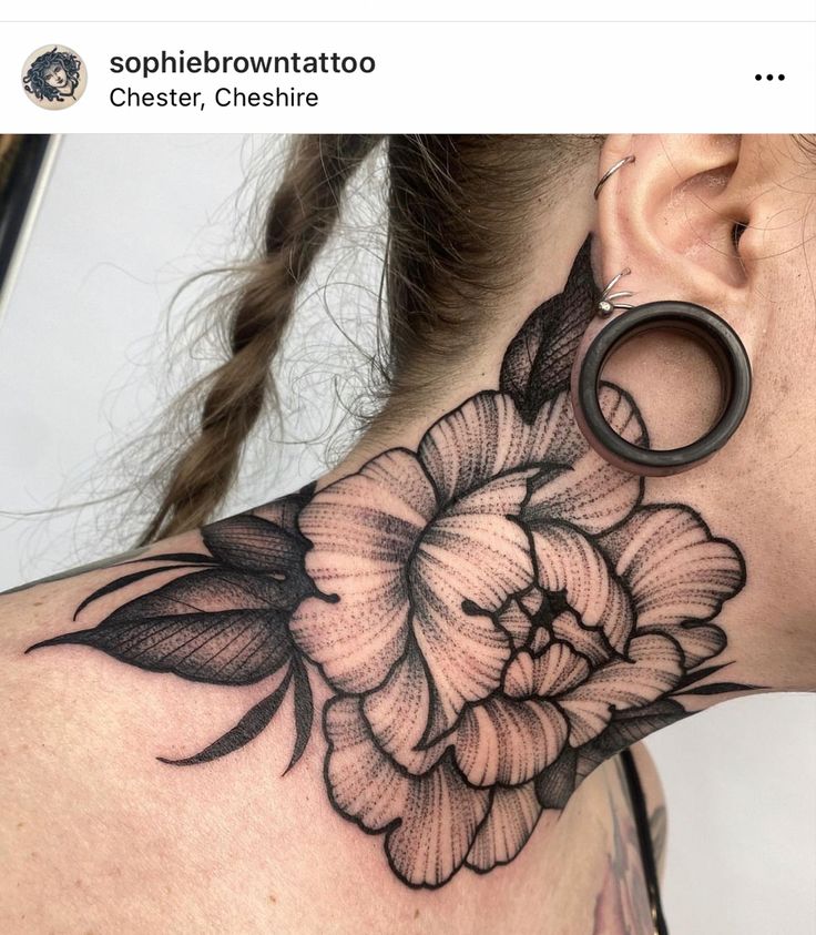 a woman's neck with a flower tattoo on the back of her neck and behind it is a pair of scissors