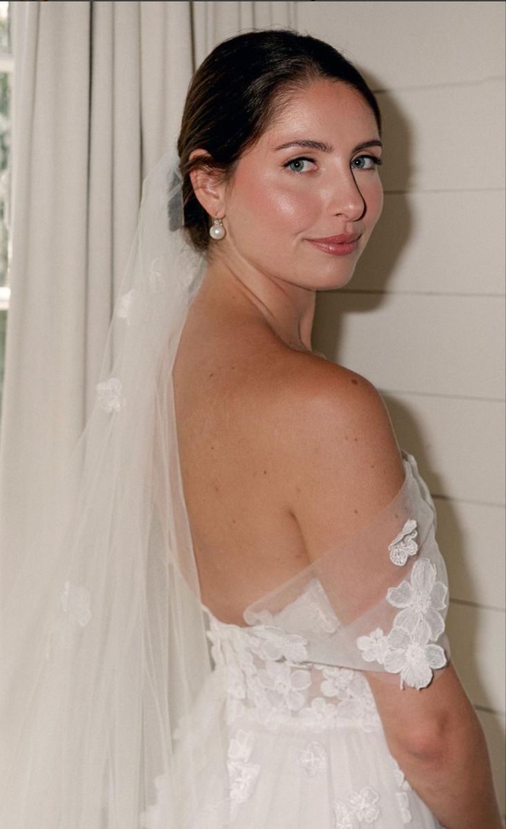 a woman in a wedding dress standing next to a window with her veil pulled back