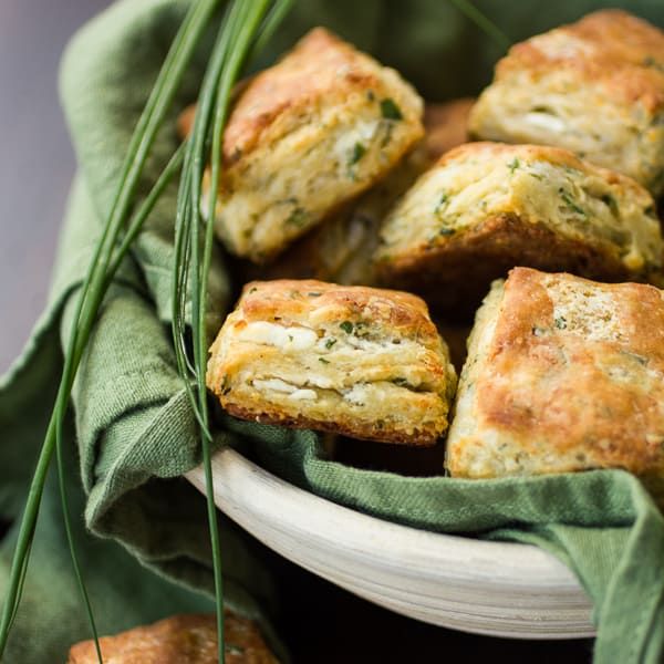 a white bowl filled with cheesy scones on top of a green cloth