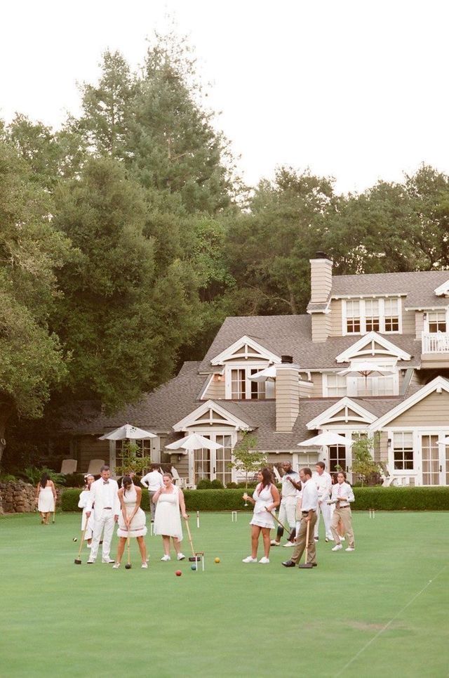 a group of people standing on top of a lush green field next to a house