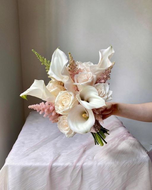 a bridal bouquet with white and pink flowers is held by someone's hand