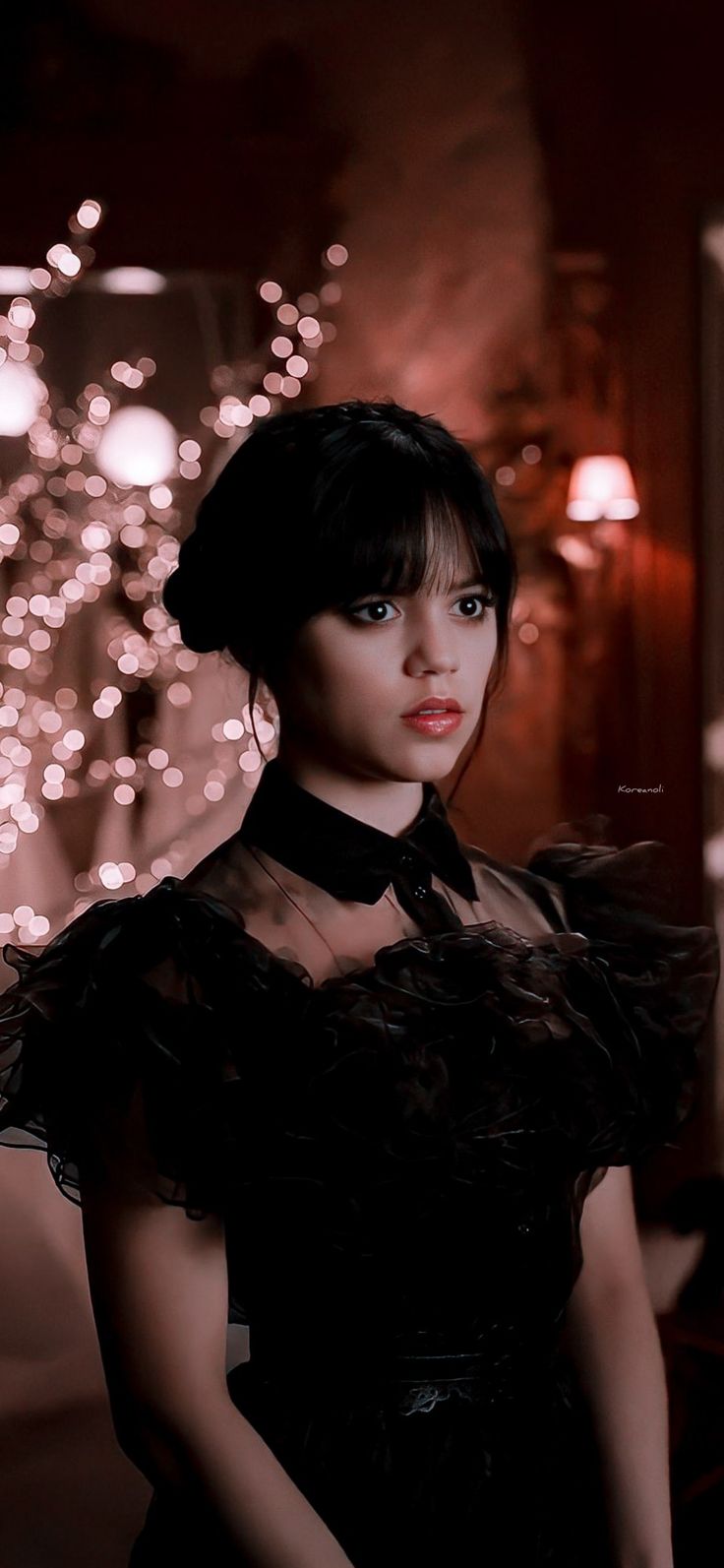 a woman in a black dress with feathers on her neck and dark hair, posing for the camera