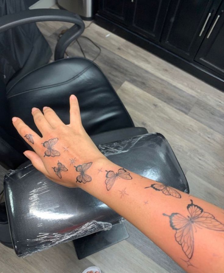 a woman's arm with butterfly tattoos on it, sitting in front of a chair