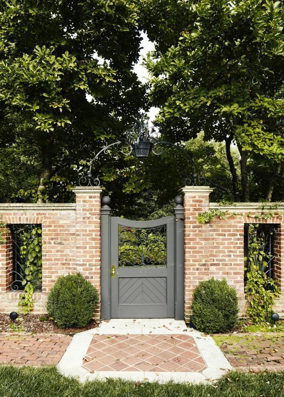 an entrance to a brick house with a gate and two bushes in the foreground