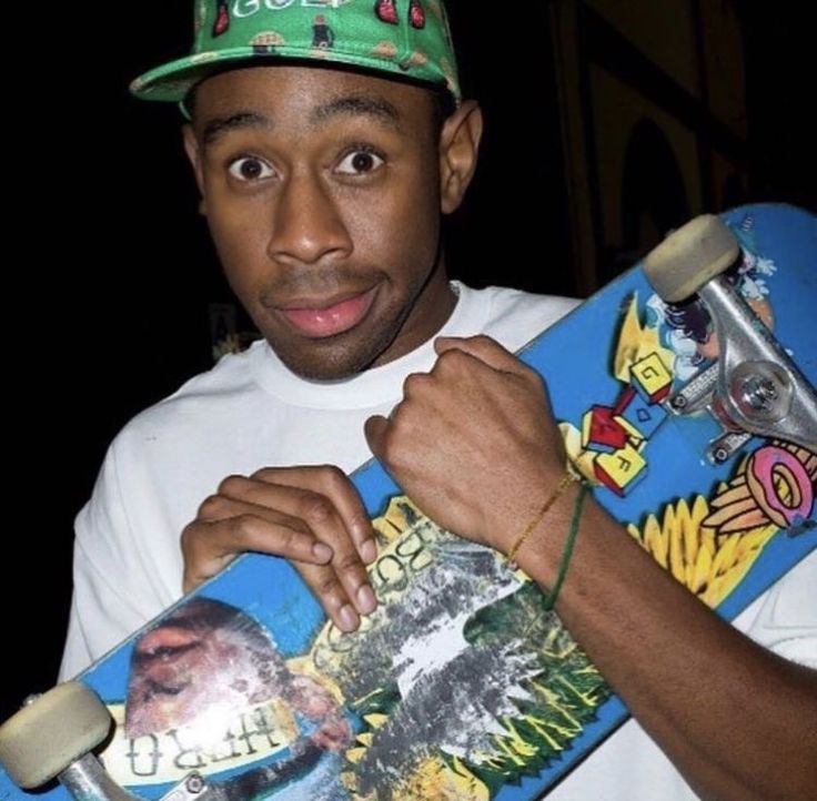 a young man holding a skateboard in his right hand and wearing a green hat