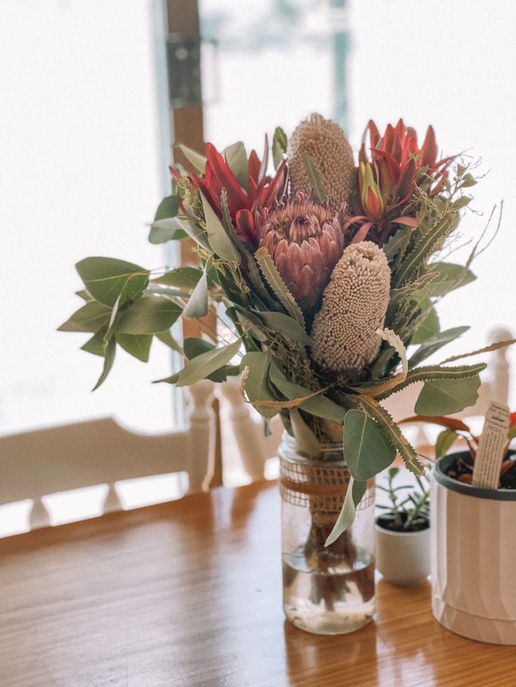 a vase filled with flowers sitting on top of a wooden table next to a potted plant