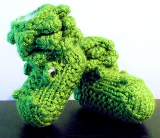 two green crocheted baby shoes sitting on top of a black table next to each other