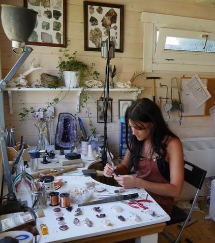 a woman is sitting at a table working on some art work in her home studio