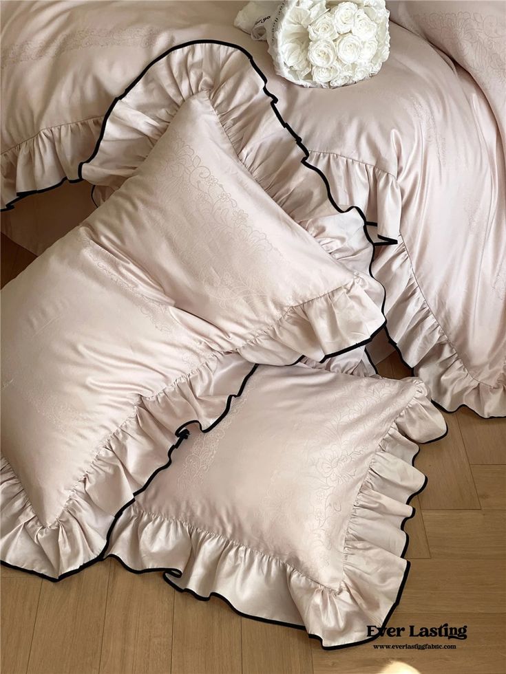 a white flower sitting on top of a bed next to two pillows and sheets with ruffled edges