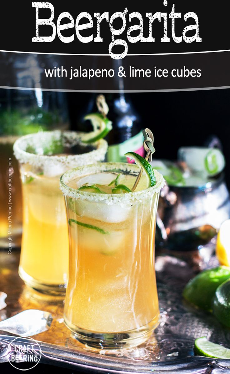 two glasses filled with drinks sitting on top of a metal tray next to limes