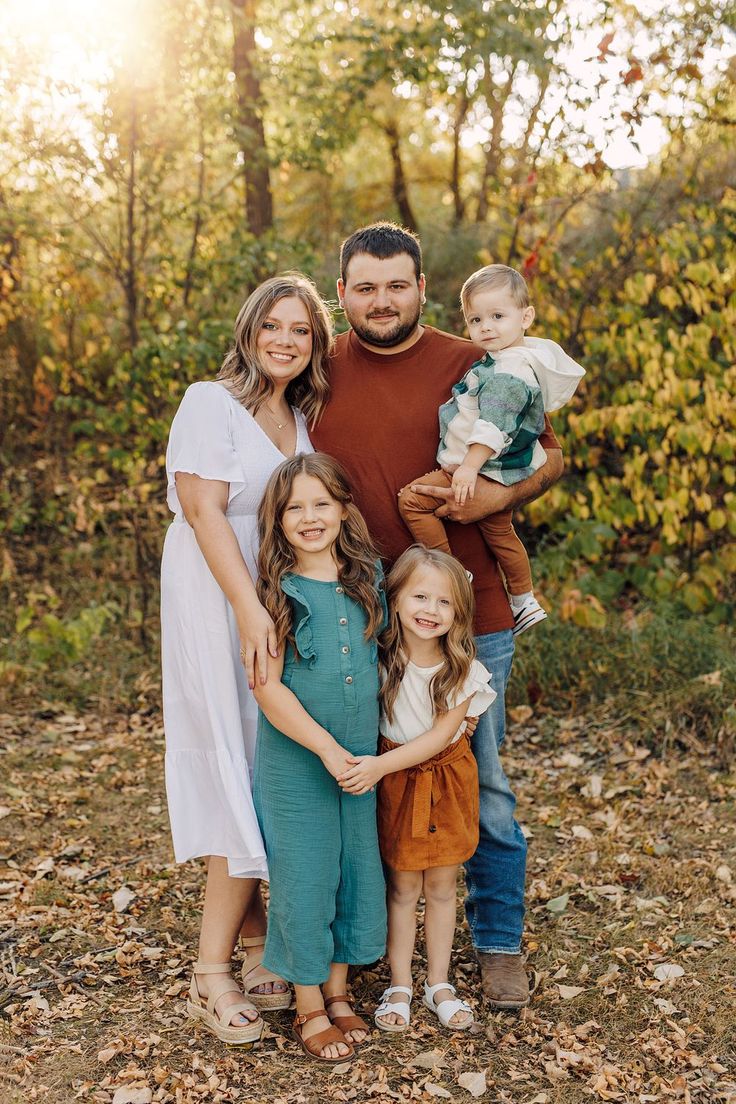 a family posing for a photo in the woods with leaves on the ground and trees behind them