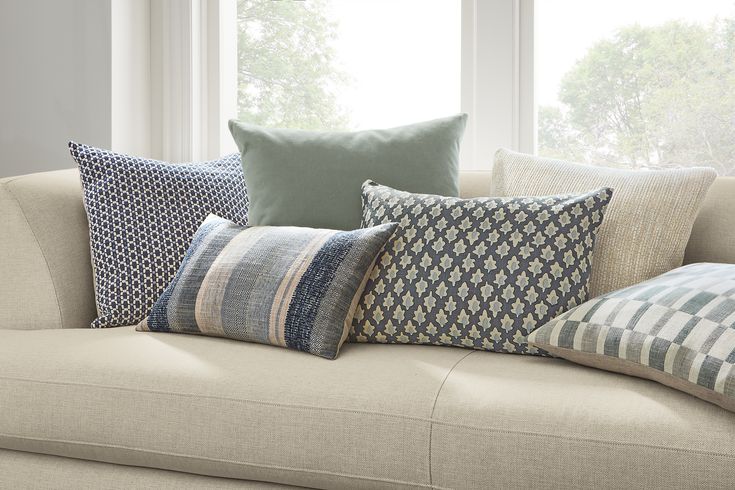 a couch with several pillows on it in front of a window and some windowsills