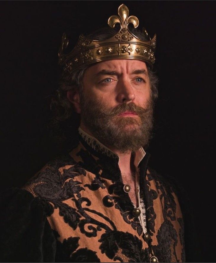 a man with a crown on his head wearing a gold and black shirt in the dark