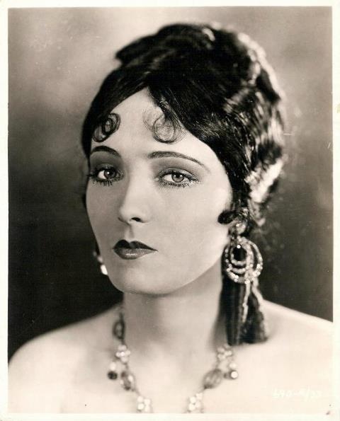 an old black and white photo of a woman with large earrings on her head, looking at the camera