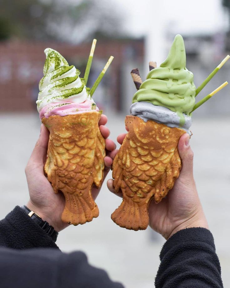 two people holding ice cream cones with green and pink toppings on them in their hands