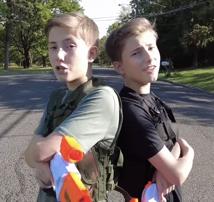 two young boys standing next to each other in the street with their arms around each other