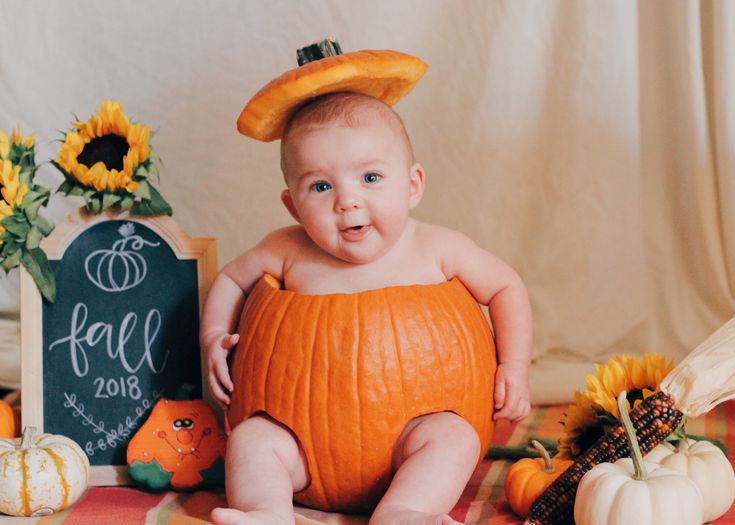 a baby in a pumpkin costume sitting on a table with sunflowers and other fall decorations