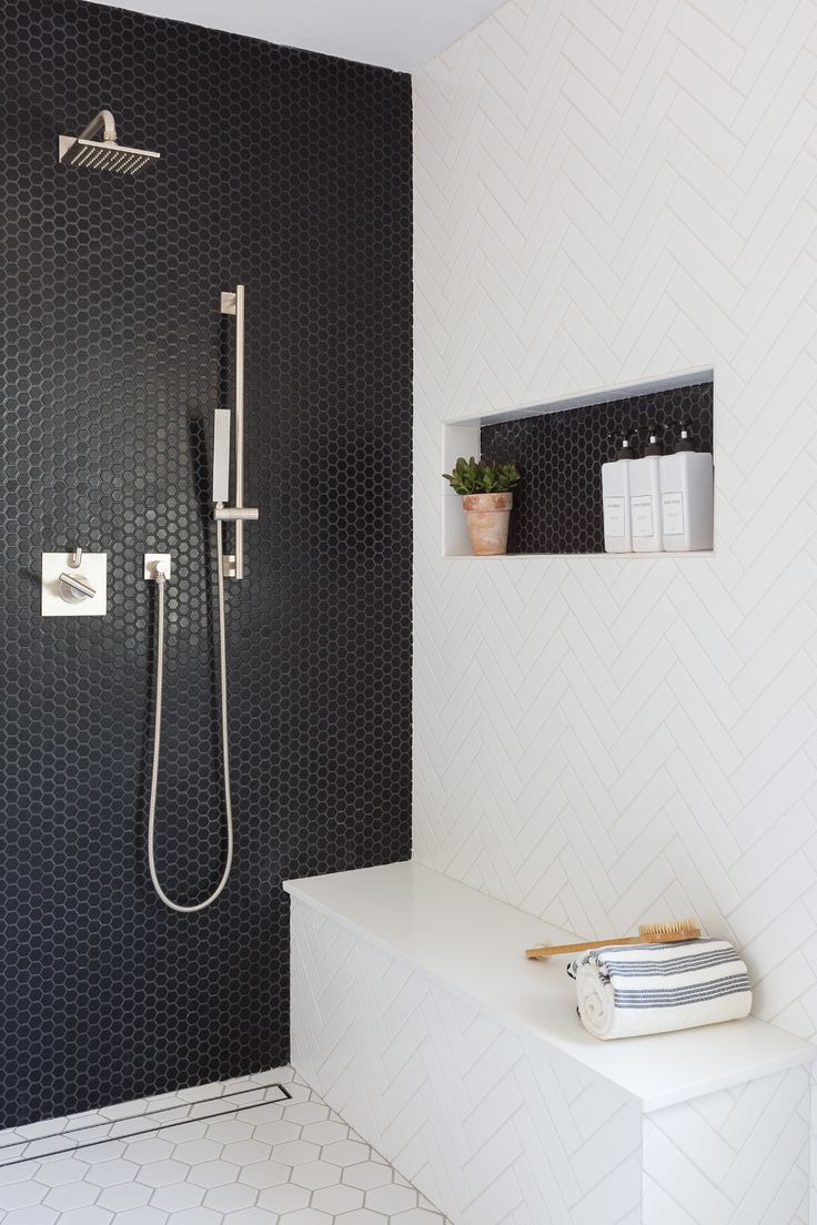 a modern bathroom with black and white tiles on the walls, shower head, and shelf