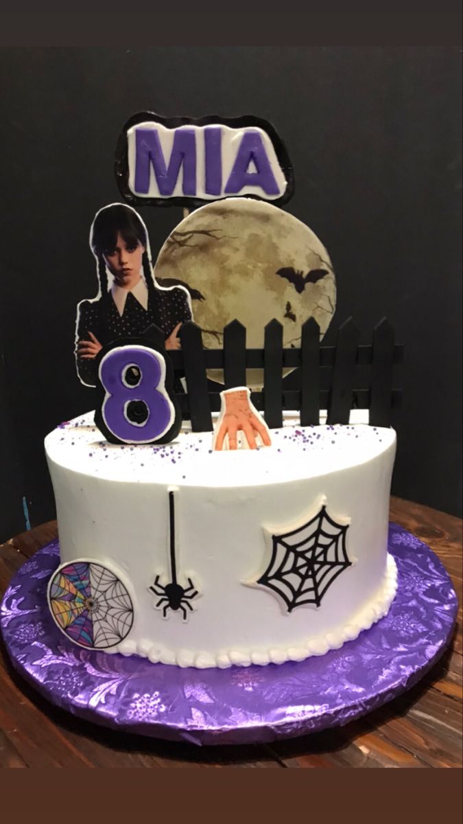 a white cake with purple icing and decorations on it, sitting on top of a wooden table