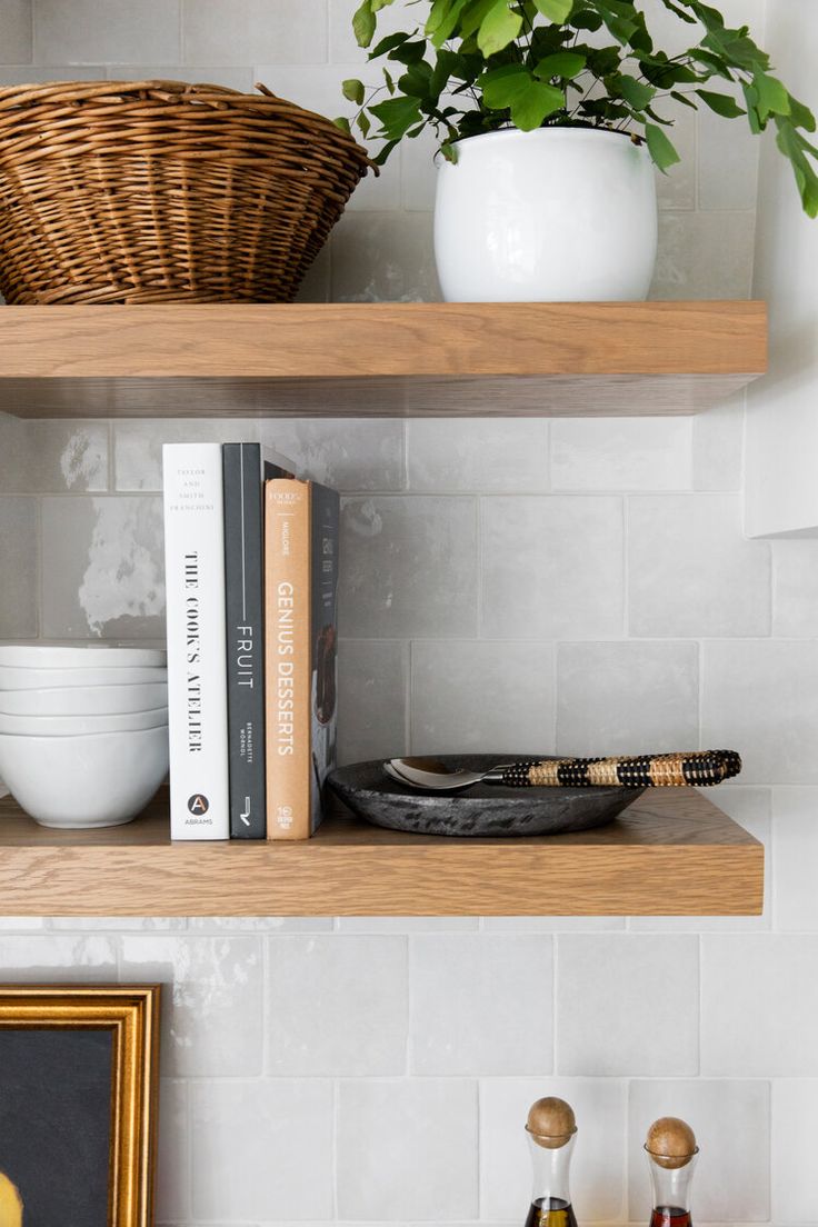 two shelves with books, bowls and plants on them in a white tiled kitchen area