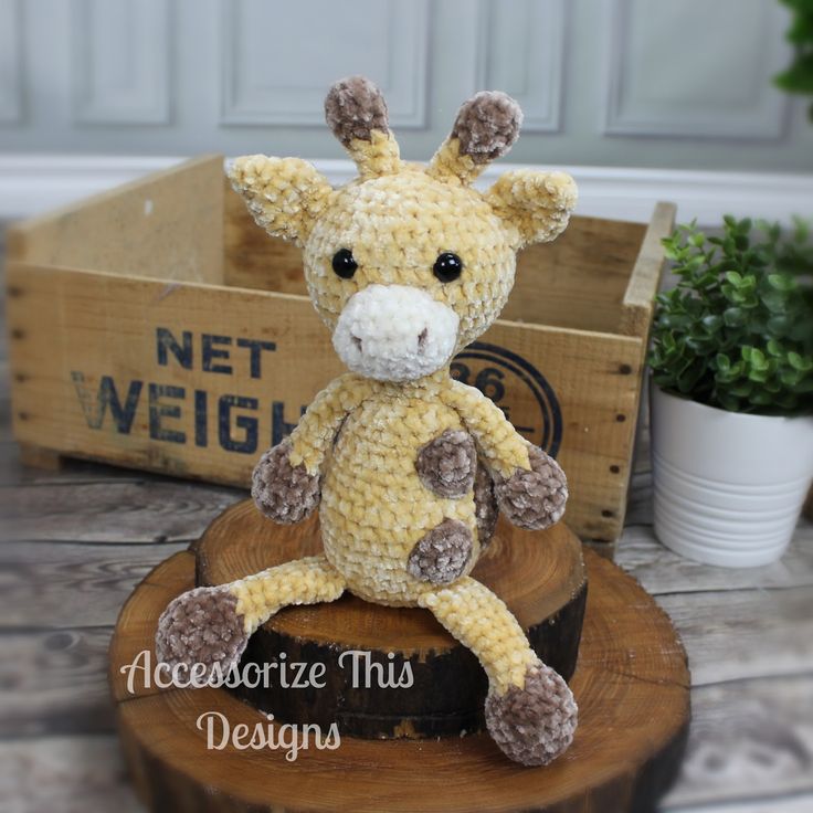 a crocheted giraffe sitting on top of a wooden stump next to a plant