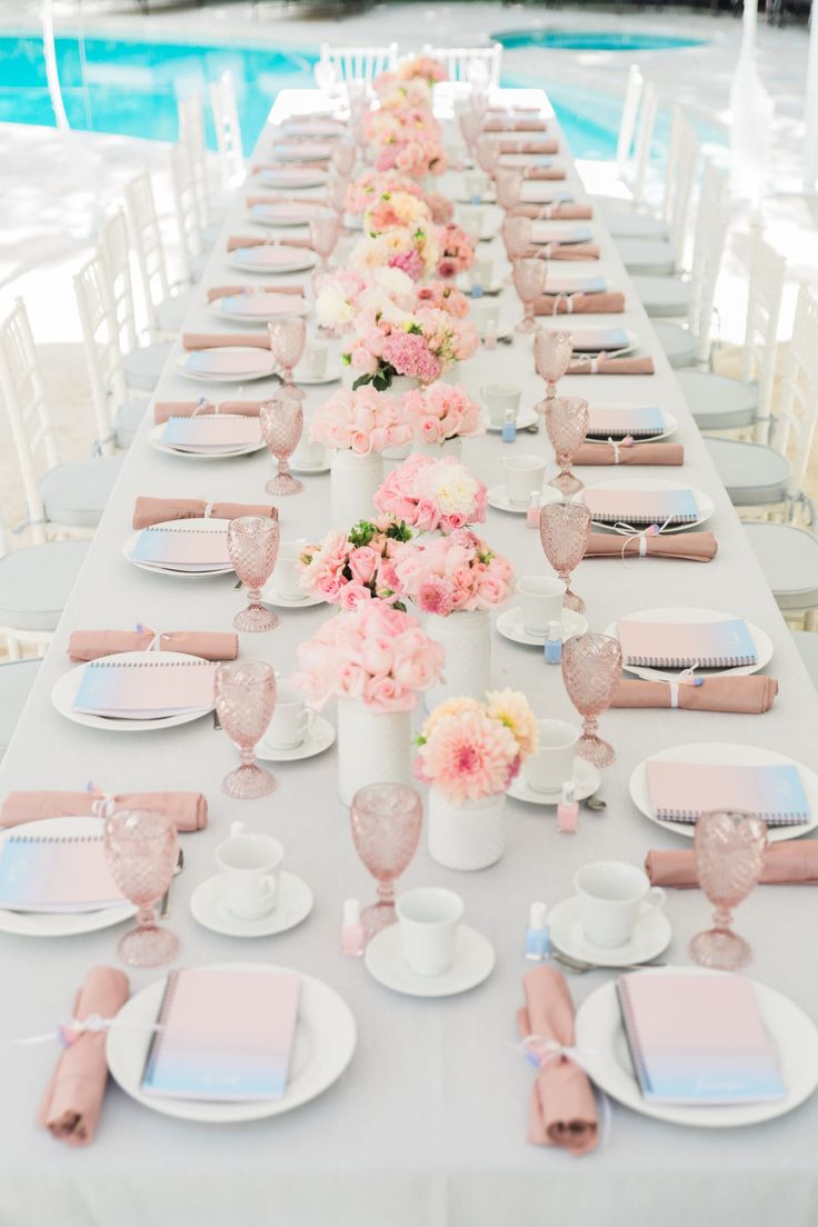 a long table set up with pink and white plates, napkins and flowers in vases