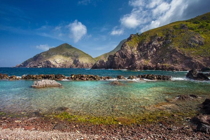 the water is crystal blue and clear with some rocks in front of it that are surrounded by mountains