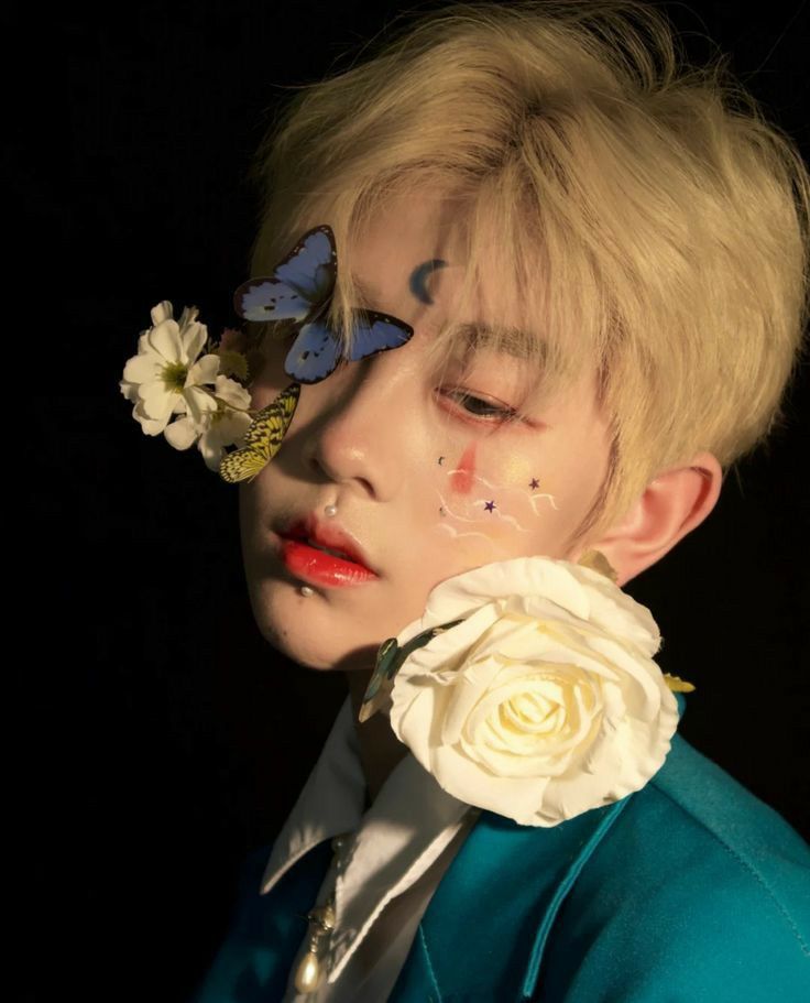 a person with flowers in their hair and a butterfly on his nose, wearing a blue jacket