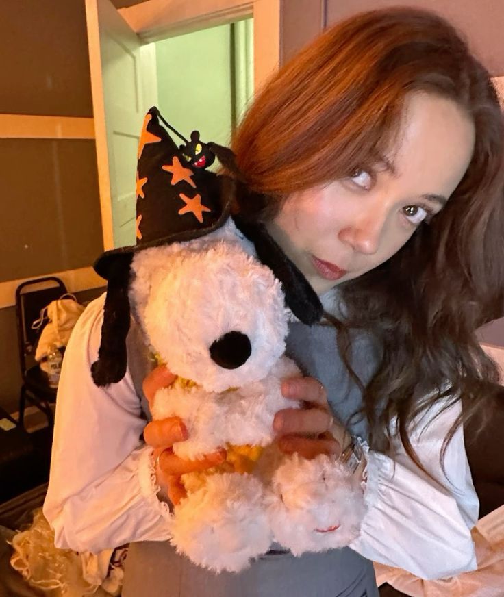 a woman holding a white teddy bear wearing a witch's hat on top of her head