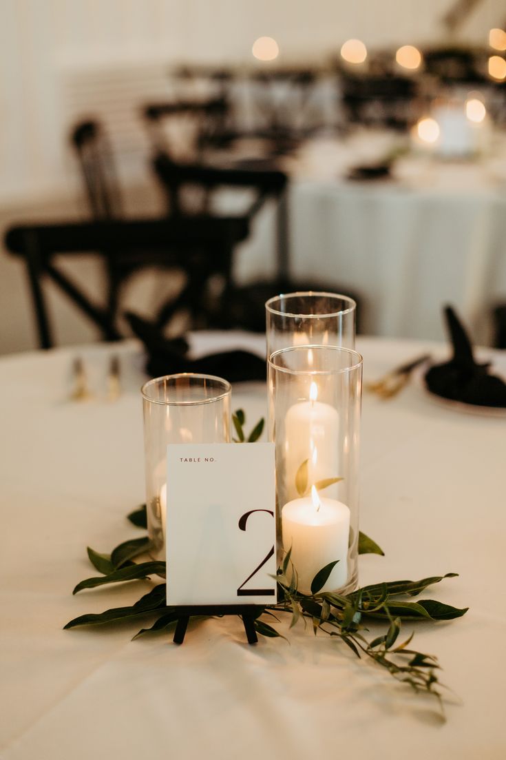 A romantic grouping of hurricane candles on top of  sprigs of greenery is a perfect touch to this elegant and modern wedding reception.

- Olivia Doerfler Photography Simplistic Table Decor Wedding, Greenery For Wedding Tables, 3 Candle Centerpiece, Candle Decor Wedding Tables, Modern Simple Wedding Decor, Wedding Table Decorations Simple Elegant, Simple Greenery Wedding Decor, Minimal Reception Decor, Simple Wedding Table Decor Candles