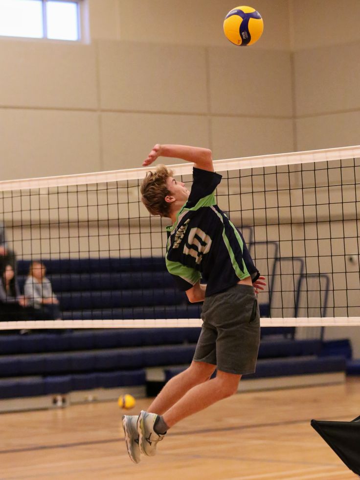 a boy jumping up to hit a volley ball with his racket in the air