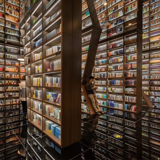 people are looking at books on shelves in a library that is filled with many different kinds of books