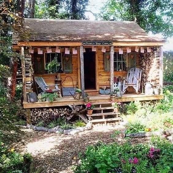 a small log cabin in the woods with chairs on the porch and steps leading up to it