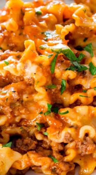 a white plate topped with pasta covered in cheese and meat sauce, garnished with parsley