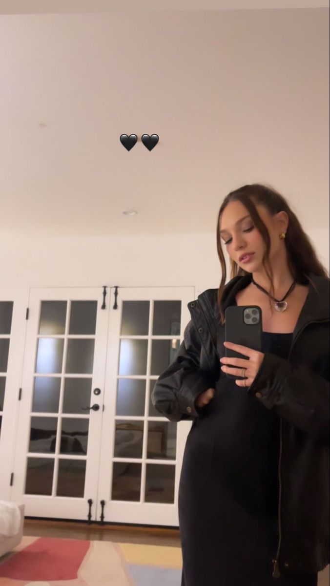 a woman in a black dress is looking at her cell phone while standing on the floor