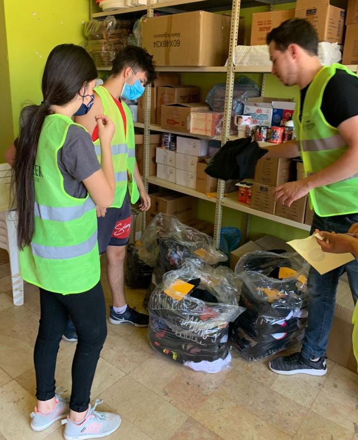 three people in yellow vests and masks looking at boxes