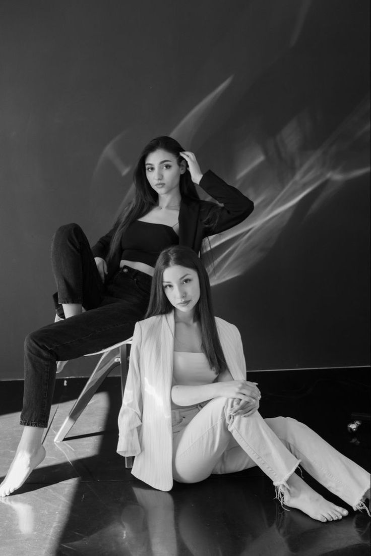 two women sitting on the floor in front of a black and white background, one with long hair