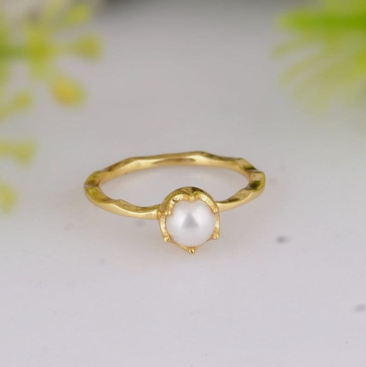 a gold ring with a white pearl in the middle and a green plant behind it