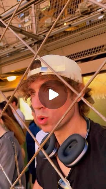 a young man wearing headphones behind a wire fence with people in the back ground