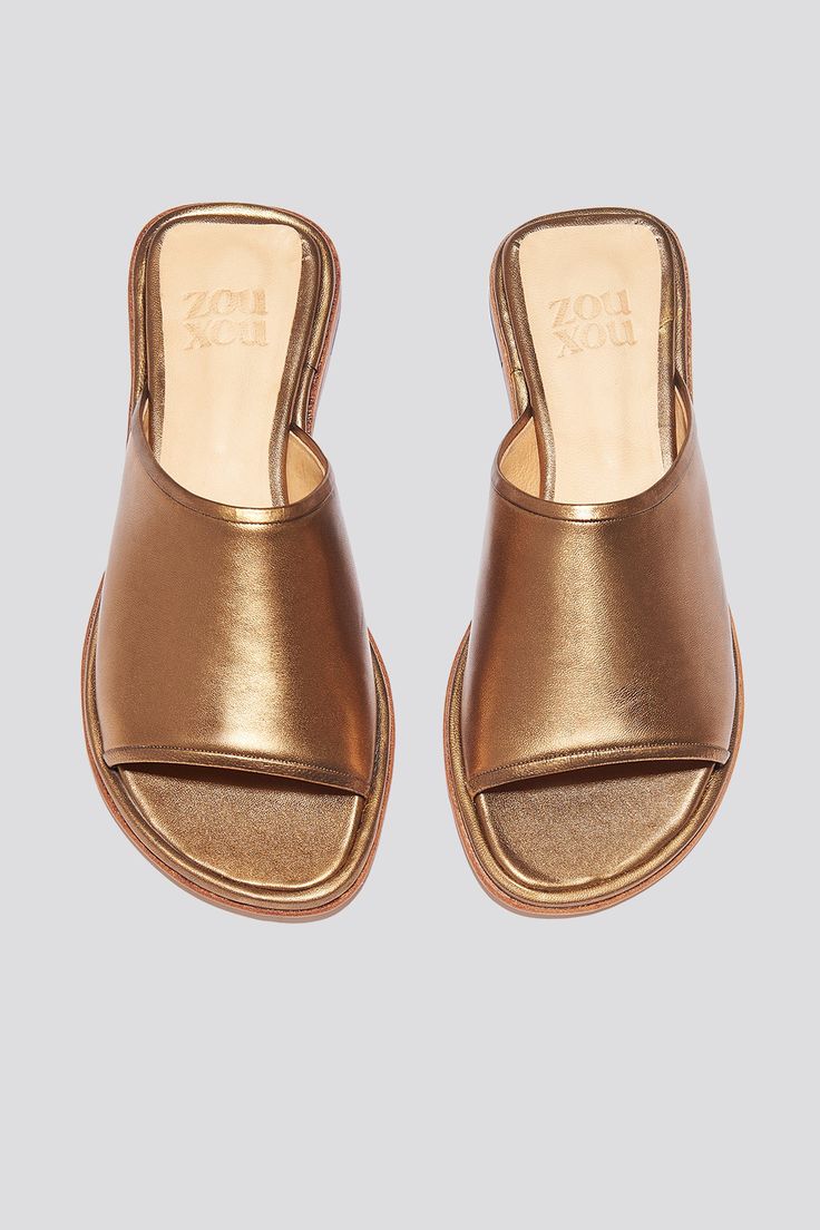 The Pileta slide is a streamlined version of the Pileta Sport Slide, featuring a sleek leather sole. The absence of details creates the perfect canvas for metallic bronze kidskin to shine. Slipping into a simple flat sandal in a striking material can be the answer to "dressing up" on a summer night when paired with a long strappy dress. Who it’s for: The woman who likes being the most comfortable person at the party.Kidskin upper with vegetable tanned leather lining and a 25 mm stacked leather h Sleek Metallic Sandals For Summer, Gold Slide Mules For Summer, Metallic Leather Sandals With Single Toe Strap, Classic Gold Sandals With Leather Footbed, Gold Leather Open Toe Slides, Gold Open Toe Leather Slides, Gold Leather Footbed Slides, Gold Slip-on Slides With Leather Footbed, Gold Leather Slides With Leather Footbed