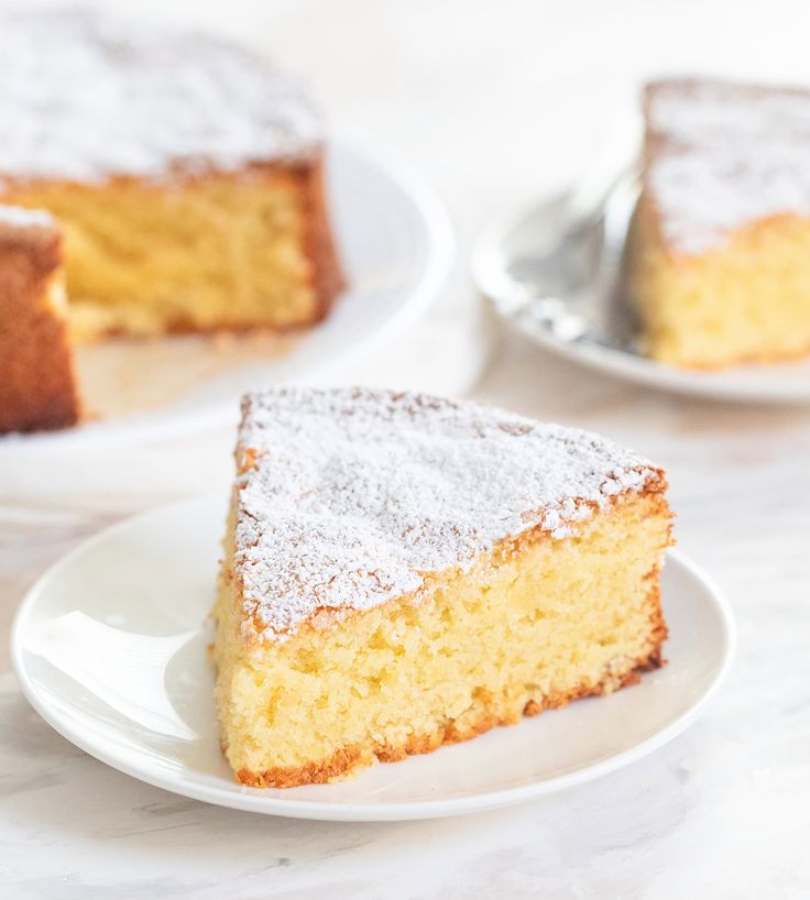 a slice of cake on a white plate with powdered sugar and two forks in the background