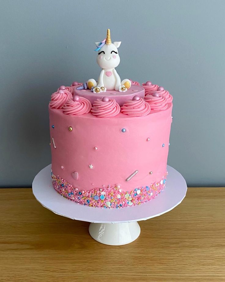 a pink birthday cake decorated with sprinkles and a unicorn figure on top