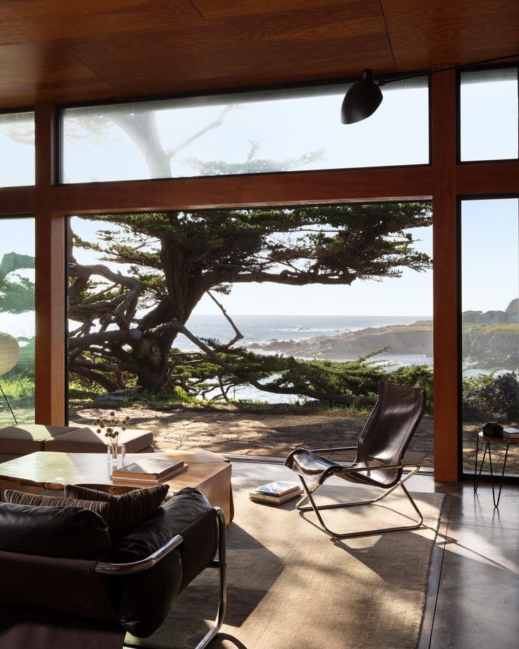 a living room with large windows overlooking the ocean and trees on the side of the house